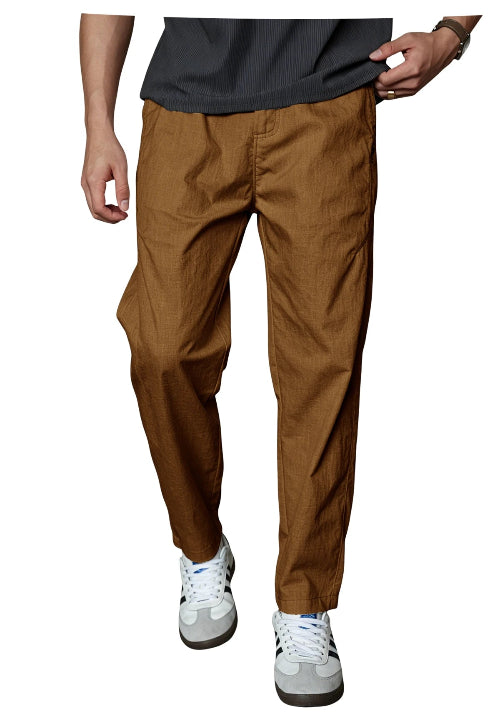 A person wearing brown tapered pants with a dark gray ribbed t-shirt and white sneakers, shown from the waist down against a plain white background.