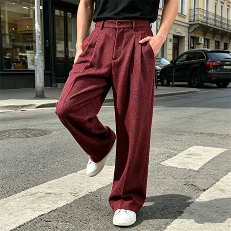 Burgundy wide-leg pleated pants worn by a man crossing a street