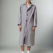 Person wearing a long gray coat on a plain background