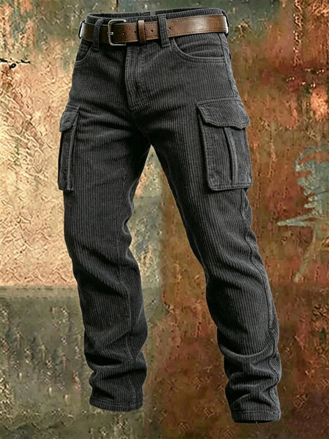 Dark gray corduroy cargo pants with flap thigh pockets and a brown belt against a textured rust-colored metal background.