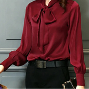 Woman wearing a burgundy blouse with a large bow tie against a gray wall.
