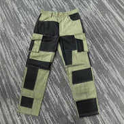 Front view of olive green and black color-block cargo pants laid flat on a gray patterned surface, showing belt loops, a button waistband, and flap thigh pockets.⠋