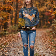 A woman wearing a long-sleeve crewneck sweatshirt with a detailed fantasy print of a fox in a starry night sky over a forest, paired with blue jeans.