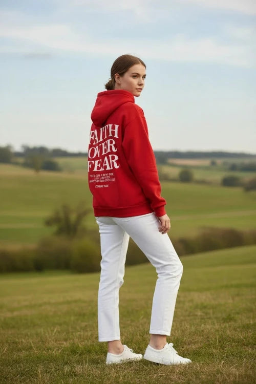 Red hoodie with 'Faith Over Fear' text on a wooden surface with shoes and headphones.