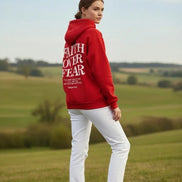 Red hoodie with 'Faith Over Fear' text on a wooden surface with shoes and headphones.
