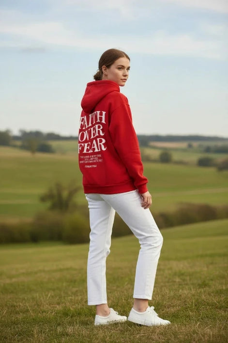 Red hoodie with 'Faith Over Fear' text on a wooden surface with shoes and headphones.