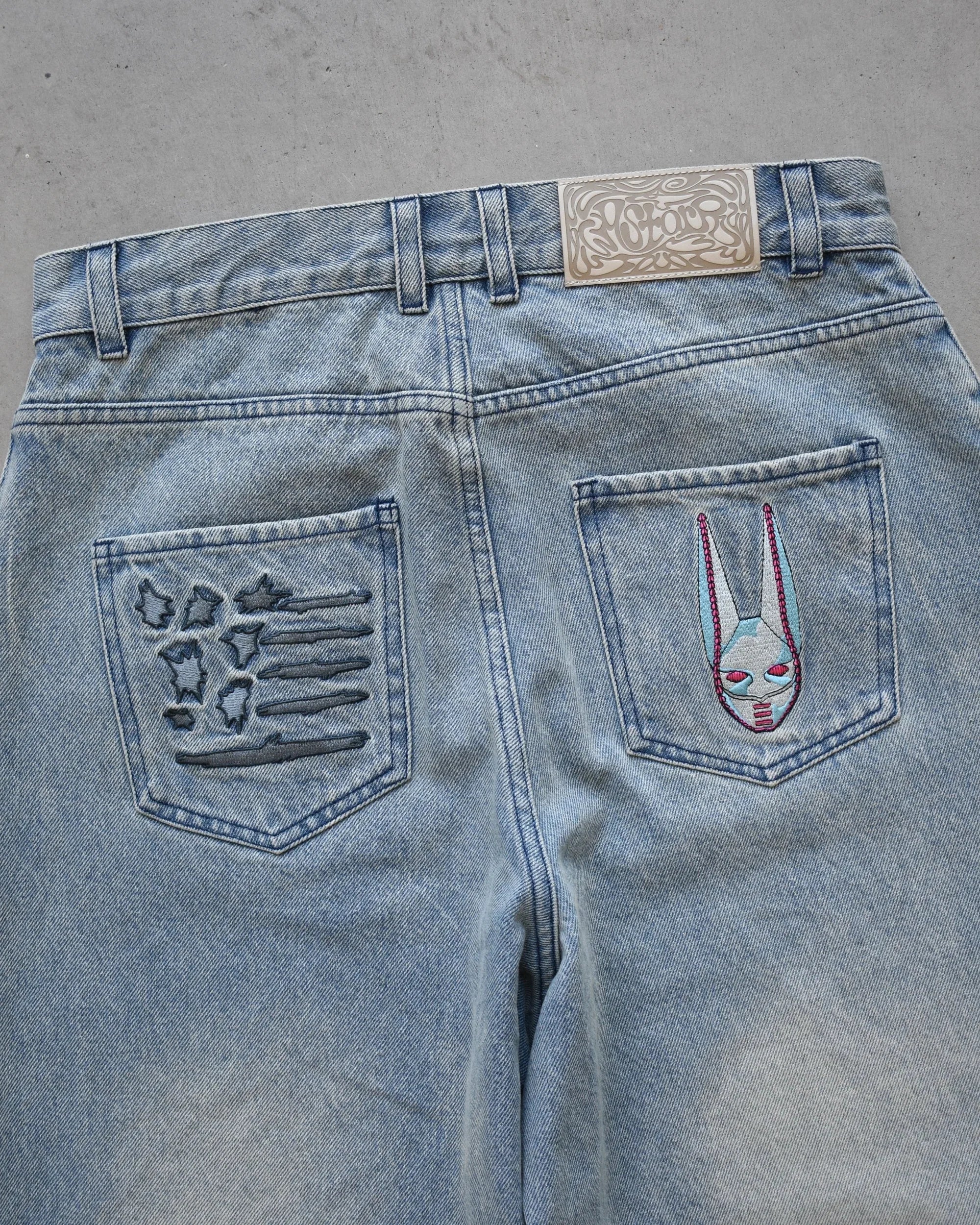 Blue jeans with embroidered designs on the back pockets against a gray background