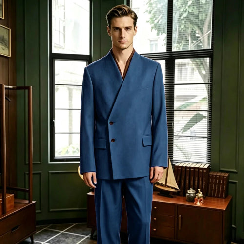 A man wearing a blue double-breasted suit with a wrap-style collar and dark brown buttons, standing in a vintage-style room with dark green walls, wooden furniture, and large windows.