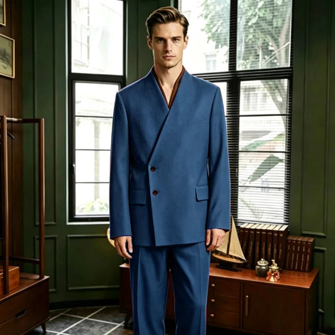 A man wearing a blue double-breasted suit with a wrap-style collar and dark brown buttons, standing in a vintage-style room with dark green walls, wooden furniture, and large windows.