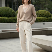 A person wearing a fuzzy beige cardigan over a ribbed beige top, standing indoors near large windows with a city view.