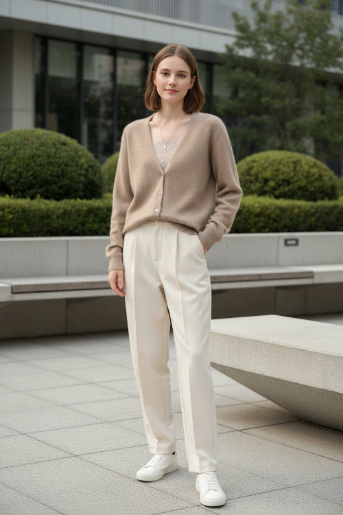A person wearing a fuzzy beige cardigan over a ribbed beige top, standing indoors near large windows with a city view.