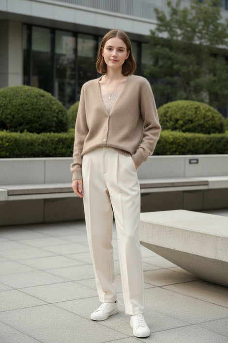 A person wearing a fuzzy beige cardigan over a ribbed beige top, standing indoors near large windows with a city view.