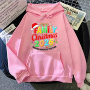 A pink pullover hoodie laid flat on a dark surface, featuring a colorful 'Family Christmas 2026' graphic 
