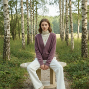 A person wearing a soft fuzzy cardigan in a muted dusty mauve-pink color over a cream turtleneck sweater 