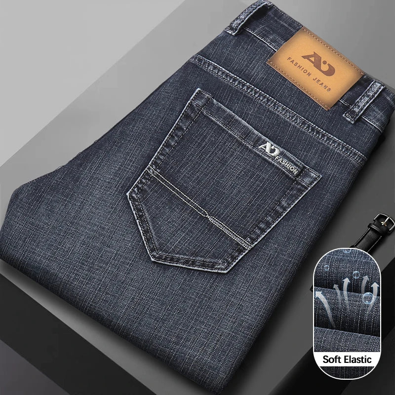 Dark gray folded denim jeans showing the back pocket, leather brand patch, and a circular inset demonstrating the soft elastic stretch.