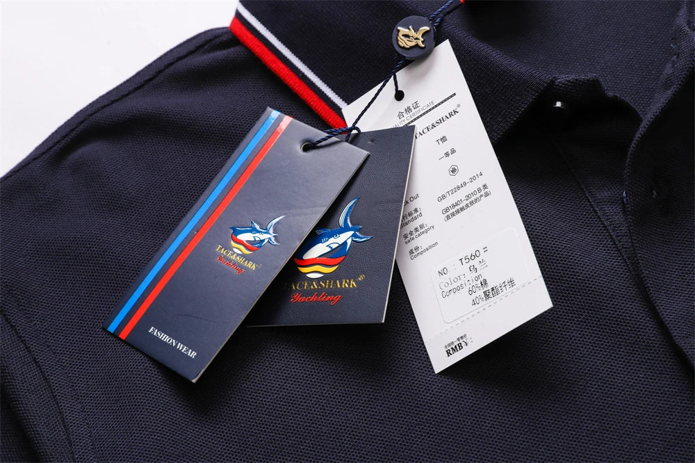 Close-up of a dark navy polo shirt fabric with a striped collar, a gold-tone button, and attached product tags including a brand tag and a white size/information tag.