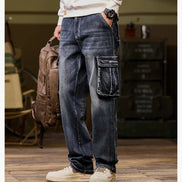 Front-angle view of a model wearing faded dark blue cargo pants with a large flap thigh pocket and one hand in a side pocket, holding a brown backpack.⠋