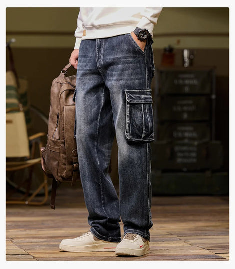 Front-angle view of a model wearing faded dark blue cargo pants with a large flap thigh pocket and one hand in a side pocket, holding a brown backpack.⠋