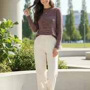 A woman wearing a marled knit mock-neck sweater in a dusty rose and burgundy tone, paired with a black skirt, standing in front of a softly lit window.