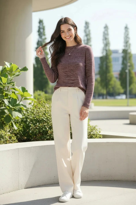 A woman wearing a marled knit mock-neck sweater in a dusty rose and burgundy tone, paired with a black skirt, standing in front of a softly lit window.