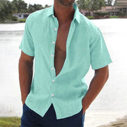 Man wearing a light green button-up shirt with short sleeves by a body of water.