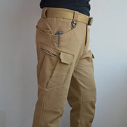 Side-angle view of a model wearing khaki cargo pants with a zippered thigh pocket, flap pocket, and matching webbing belt against a light gray background.