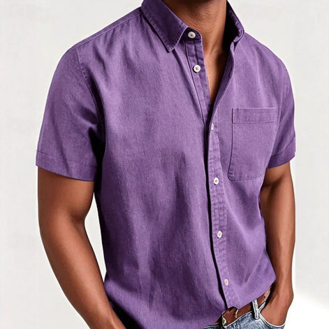 A man wearing a short-sleeve button-up shirt in a solid purple color, paired with blue jeans and a brown leather belt,