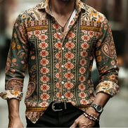 A man wearing a long-sleeve button-up shirt with an intricate multicolor bohemian paisley and floral pattern, paired with black trousers and accessories, set against a blurred urban background.