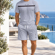 A man wearing a light gray short-sleeve t-shirt and matching patterned shorts, standing on a wooden boardwalk 