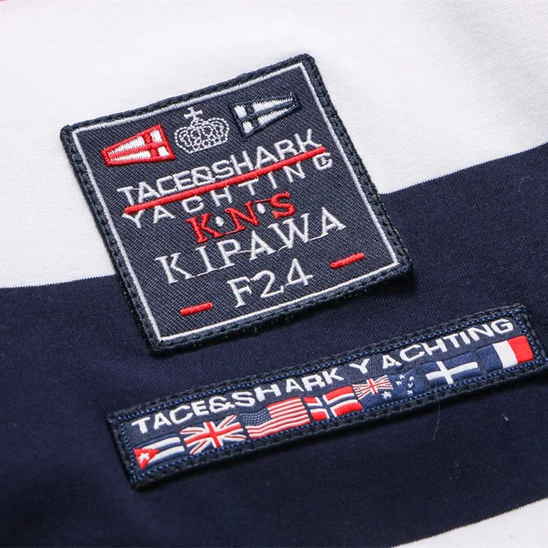 Close-up of embroidered patches on a navy and white striped garment. The top patch reads 'TACE&SHARK YACHTING K.