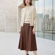 A person wearing a cream-colored knit cardigan over a matching cream sweater, paired with a brown faux-leather skirt, shown from the neck down in an indoor setting.