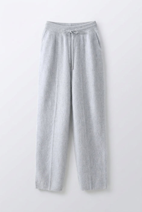 Light gray fuzzy knit lounge pants with a drawstring waist, hanging on a wooden hanger inside a dark wood and white drawer closet.
