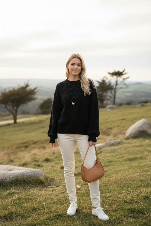 A person wearing a black cable-knit sweater with a diamond pattern, 