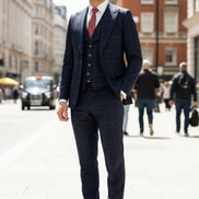 Man in a navy checkered suit with a red tie standing in an urban setting