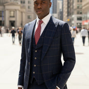 Man in a navy checkered suit with a red tie standing in an urban setting