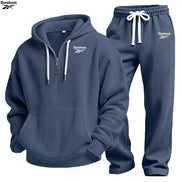 A two-piece Under Armour tracksuit set in navy blue waffle fabric, featuring a half-zip hoodie with white drawstrings and logo details, 