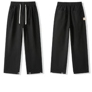 Front and back views of black straight-leg pants laid flat, showing an elastic waistband, white drawstring, slanted side pockets, and back patch pockets.