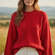 A woman wearing a bright red cable-knit sweater and white pants, holding a pearl-beaded handbag. 