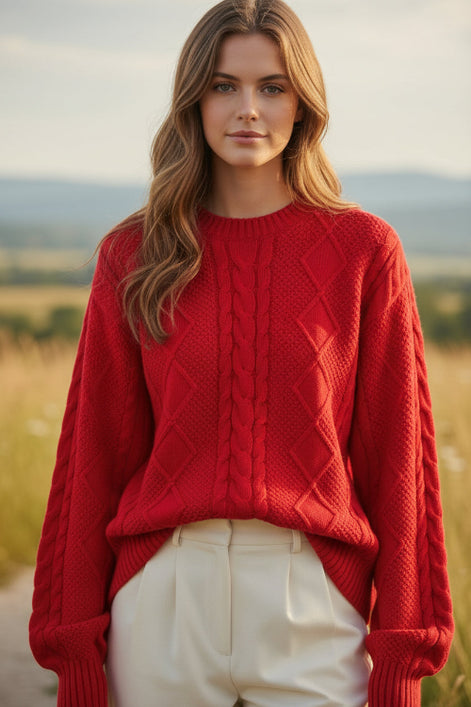 A woman wearing a bright red cable-knit sweater and white pants, holding a pearl-beaded handbag. 