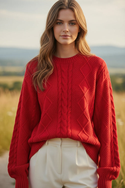 A woman wearing a bright red cable-knit sweater and white pants, holding a pearl-beaded handbag. 