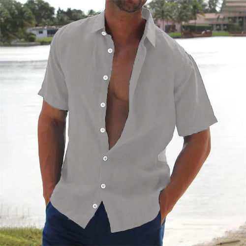 Man wearing a gray open-neck shirt with short sleeves by a body of water.