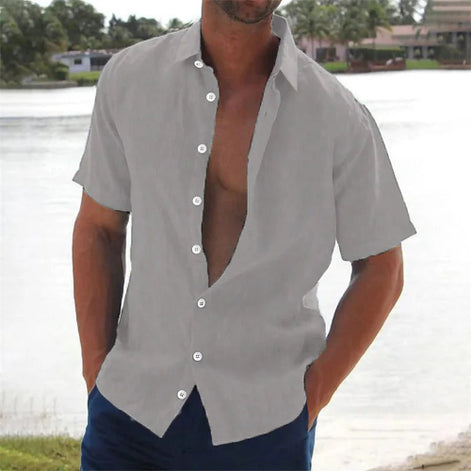 Man wearing a gray open-neck shirt with short sleeves by a body of water.