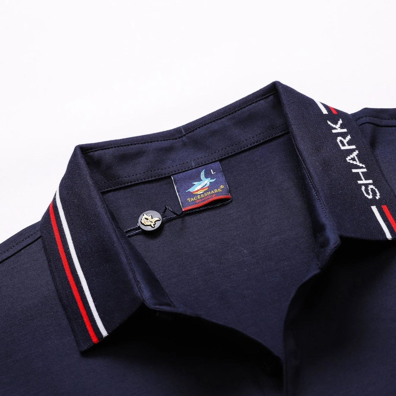 Close-up of a navy blue polo shirt collar with red and white stripe accents, a silver button, and a visible 'SHARK' neck label.