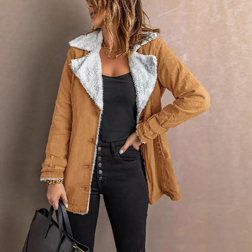 Woman wearing a tan jacket with white fleece-look lining, wide lapels and buckled cuffs over a black top and jeans