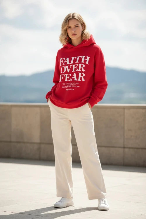 Red hoodie with 'Faith Over Fear' text on a wooden surface with shoes and headphones.
