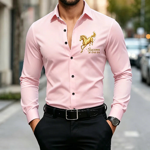 A man wearing a light pink long-sleeve button-up shirt with a gold embroidered horse and the words 'Success at first try' on the left chest, 
