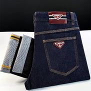 A folded pair of dark indigo denim jeans with contrast stitching and a triangular metal logo patch on the back pocket, 