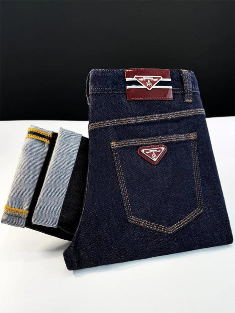 A folded pair of dark indigo denim jeans with contrast stitching and a triangular metal logo patch on the back pocket, 