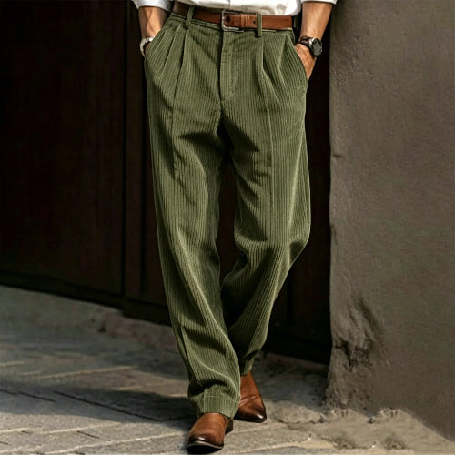 Person wearing green pleated pants and brown shoes against a textured wall.