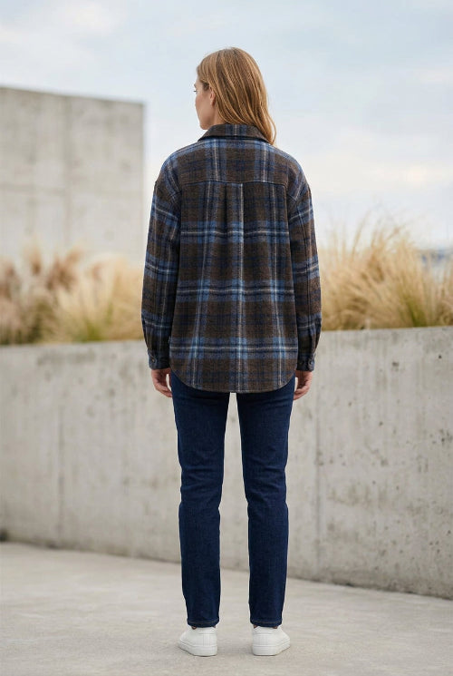 A long-sleeve plaid flannel shirt jacket in dark brown, blue, and black, hanging on a hanger on a clothing rack in a boutique.